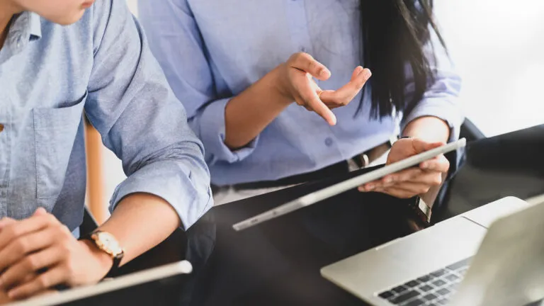 Cropped image of PEAK6 business team working together by using a computer tablet and laptop while sitting at the modern working desk over comfortable office as background.