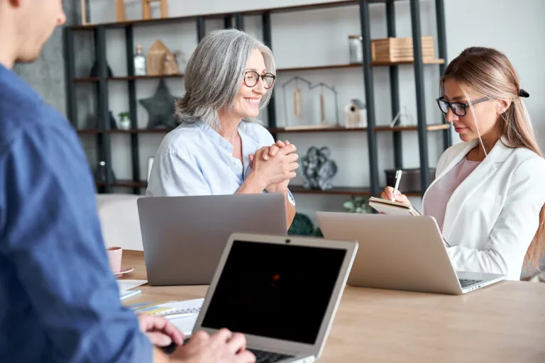 A photo of two women in an office. One woman is older and speaking to the younger woman who is taking notes.
