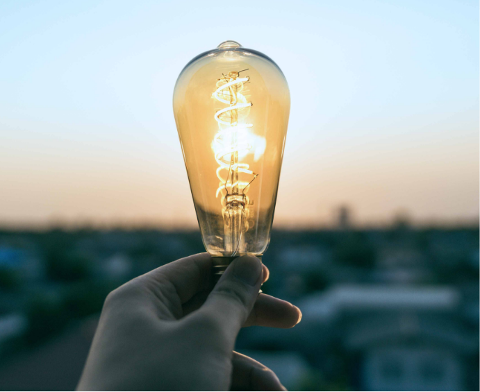 Image of a hand holding a light bulb which is inexplicably lit though not plugged in.