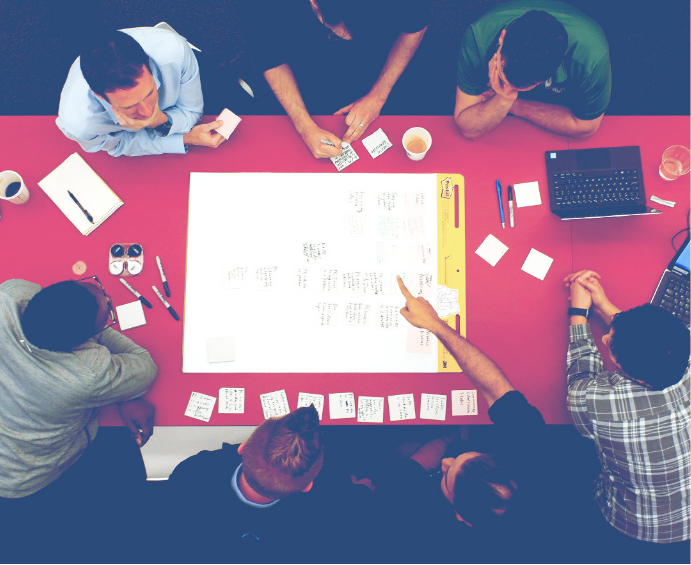 Image of seven men collaborating over a conference table, as seen from above.