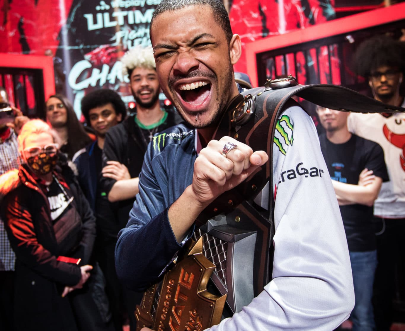 Picture of young, Black, male gamer celebrating a win while an excited crowd watches behind him.
