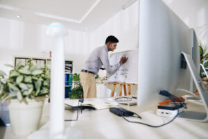 Concentrated young Indian software engineer drawing block diagram on whiteboard before starting work on programming code.