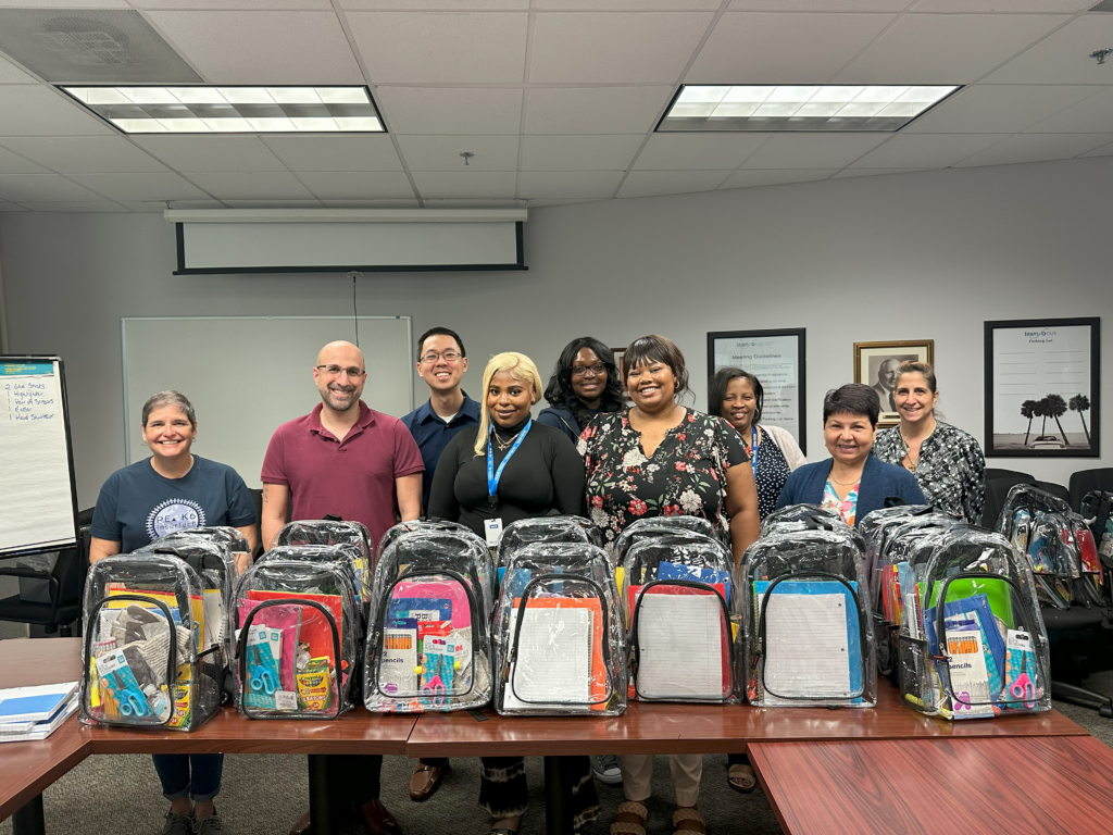 A team of PEAK6 InsurTech employees proudly displaying backpacks filled with school supplies.