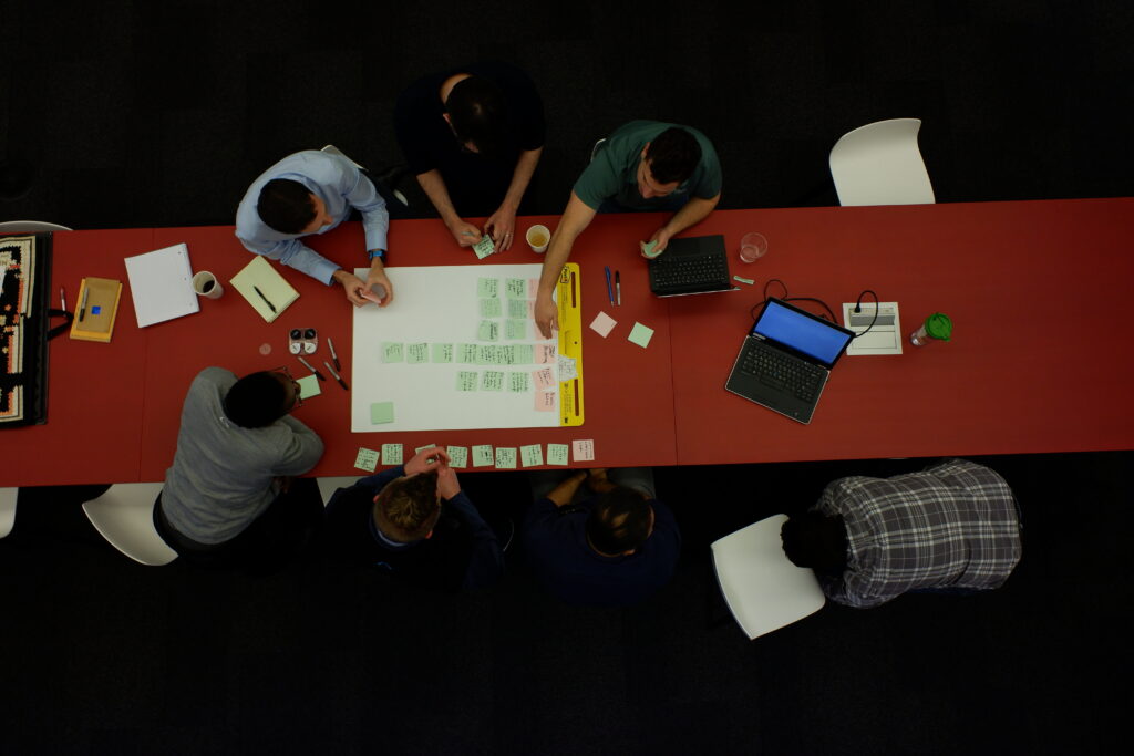 A group of PEAK6 employees gather around a large piece of paper along with many sticky notes and digital tools, planning out the next stages of their project.