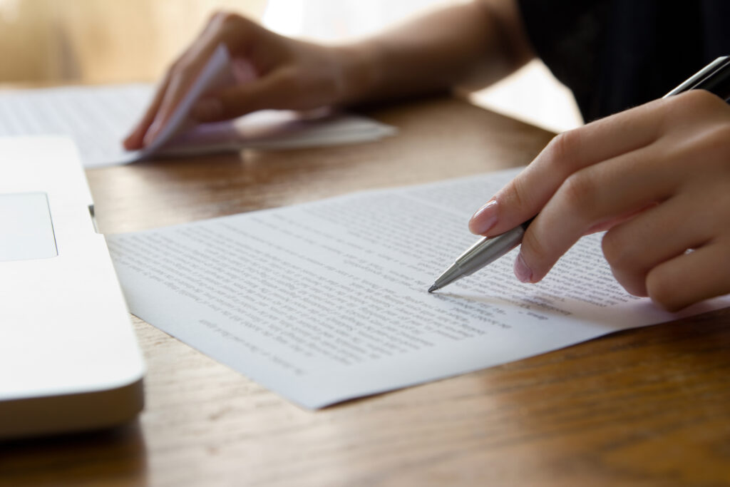 A close-up shot of someone editing a paper, they are holding a pen in one hand and flipping through documents with the other.