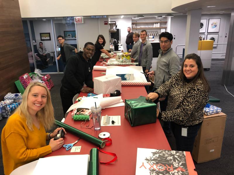 Several PEAK6 employees posing for the camera as they wrap donated holiday gifts.