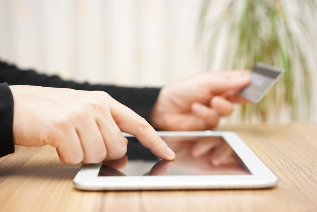 A close up photo of someone’s hands using a tablet device. One hand holding a credit card and the other is typing the information into the tablet.