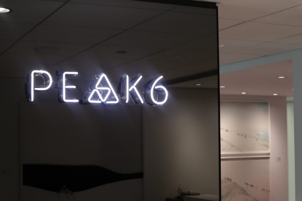 A neon sign of the PEAK6 logo with a delta replacing the “a” hanging at the entrance of the PEAK6 Chicago headquarters.